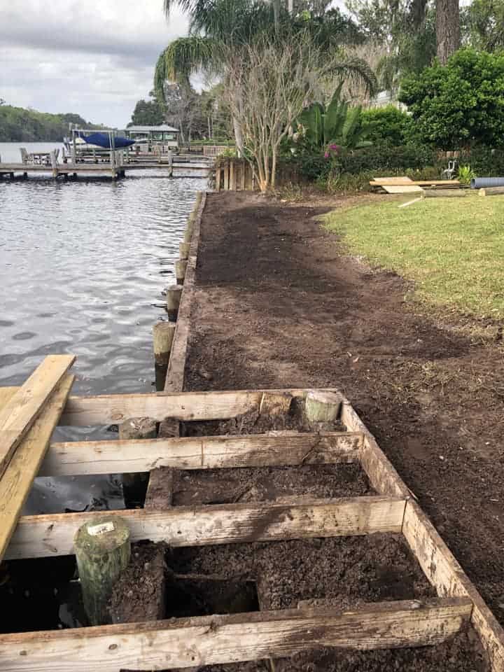 Timber bulkhead under construction along a riverbank, fresh soil backfill and open joist framing over water