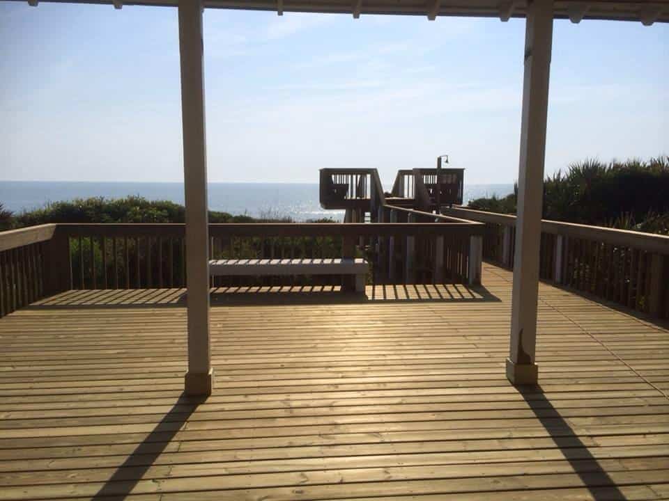 Covered wooden deck with bench and railing overlooking the ocean, walkway to an observation platform