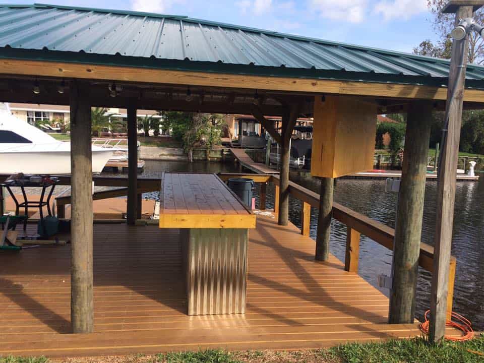 Covered dock with green metal roof, wooden bar counter on corrugated metal base, string lights