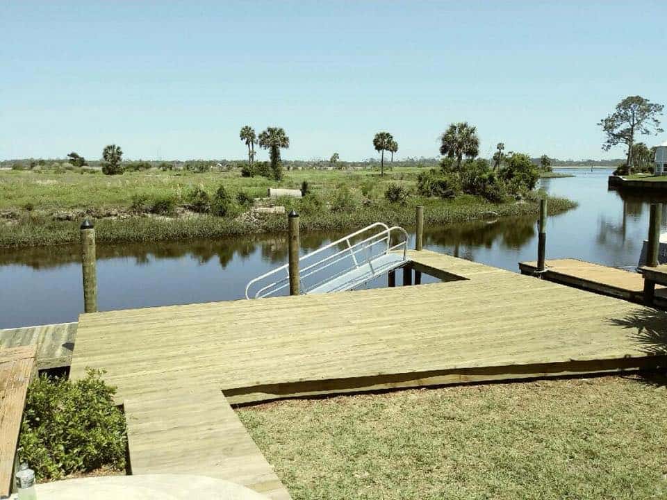 Large square wood dock platform with aluminum gangway railing beside a marsh creek and palms