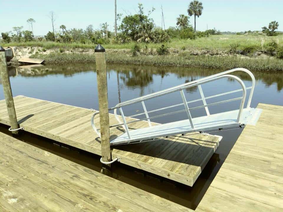 Aluminum gangway with handrails hinged between a wooden dock and floating platform on a creek