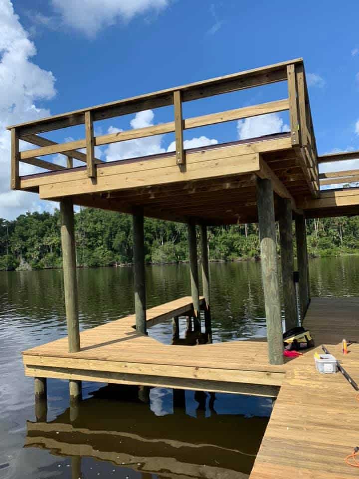 Two-story wooden dock under construction on pilings over a river, upper deck railed