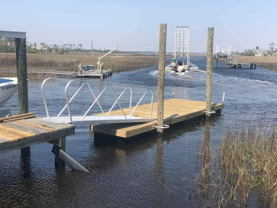 Floating dock with aluminum gangway and guide pilings in a tidal marsh creek, boats nearby