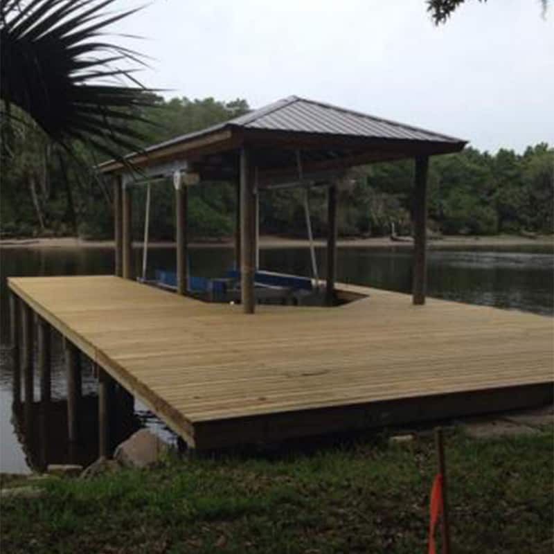 Covered boat lift with hip metal roof set into a wide wood dock deck on a river