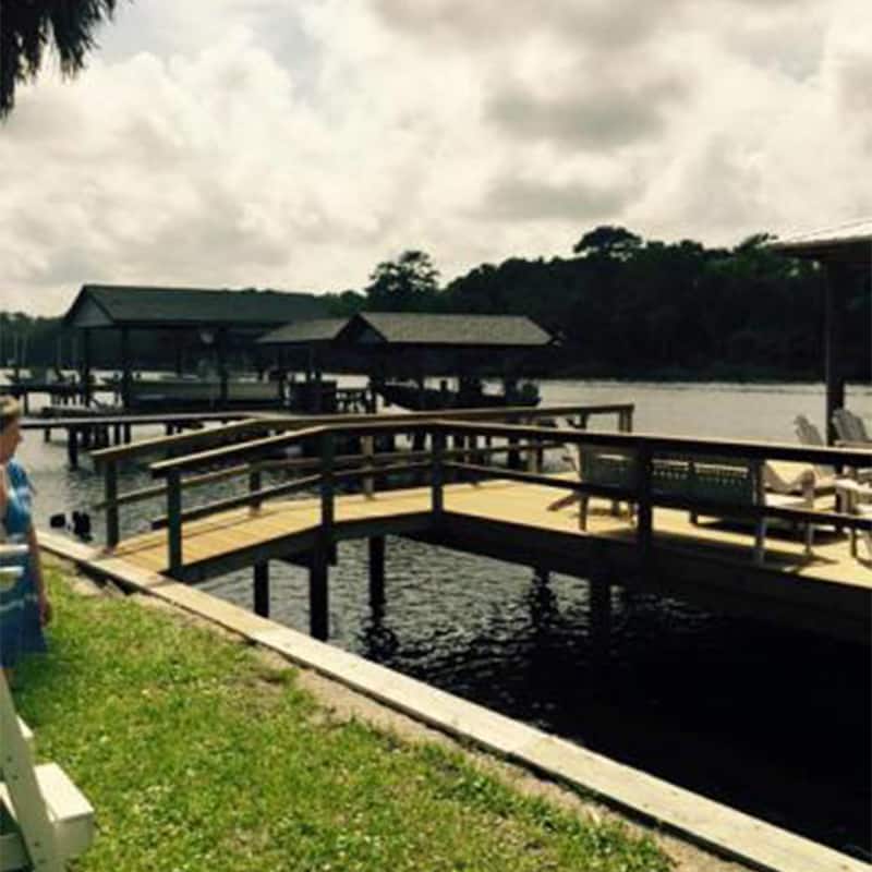 Railed wood dock with built-in benches and Adirondack chairs, covered boathouses across the water