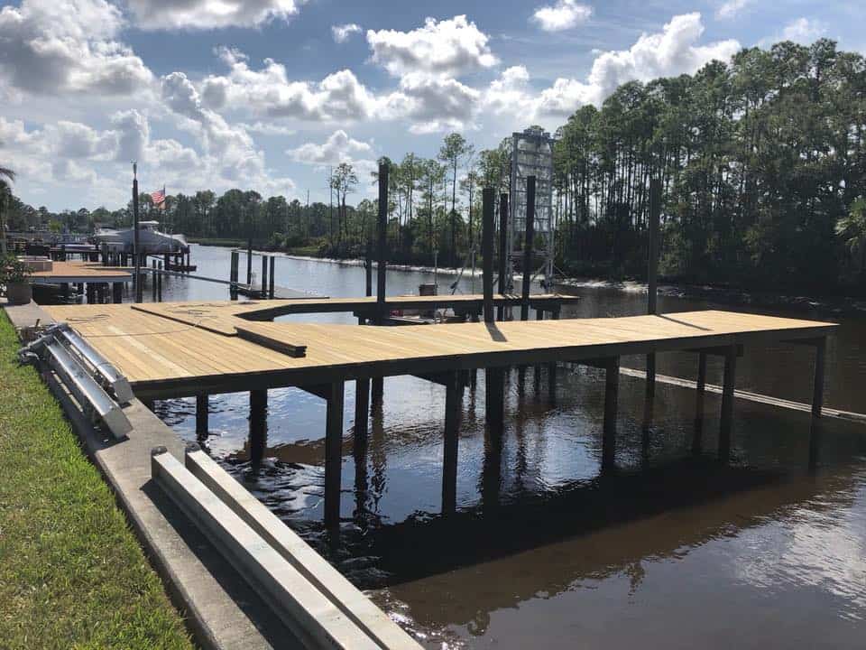 New dock decking on dark pilings over a canal, aluminum beams stacked on the bank