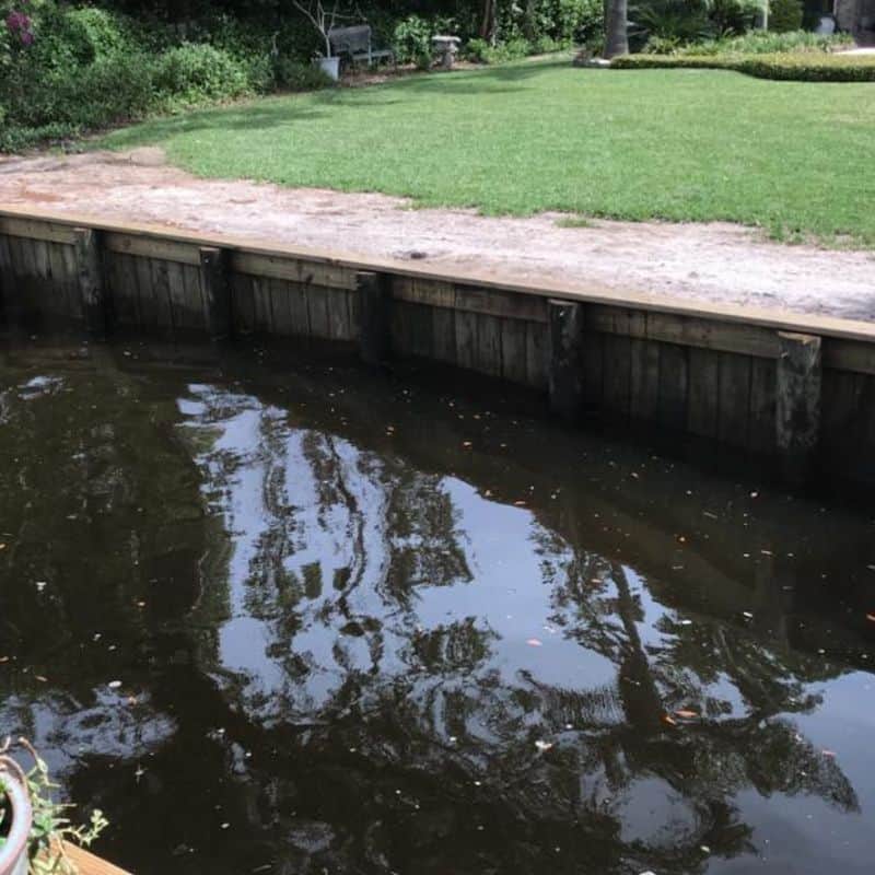 Timber seawall with capped top separating a manicured lawn from dark canal water