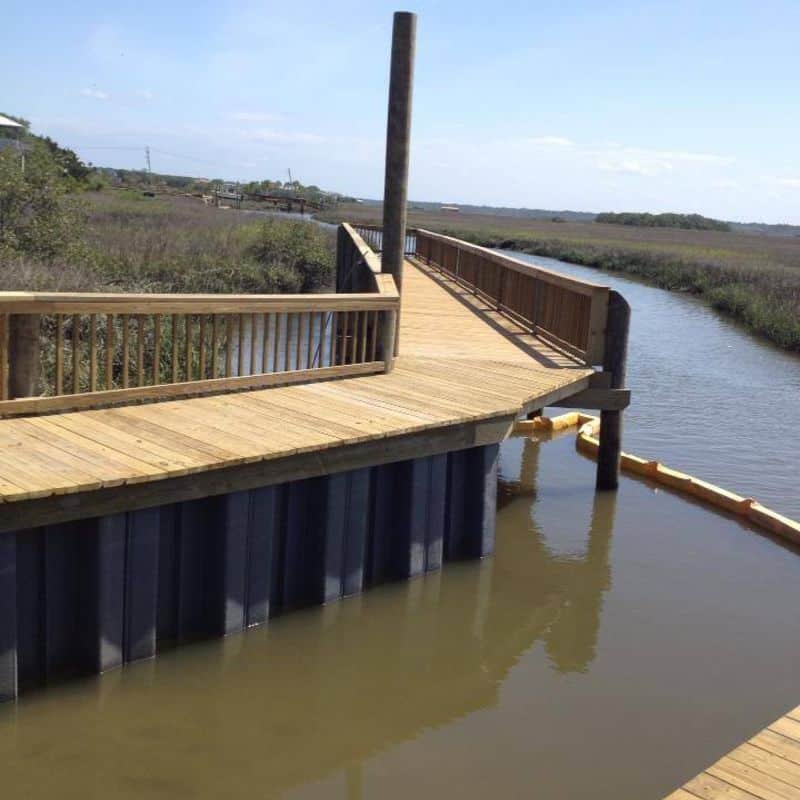 Wooden walkway on a black vinyl seawall curving along a tidal marsh creek