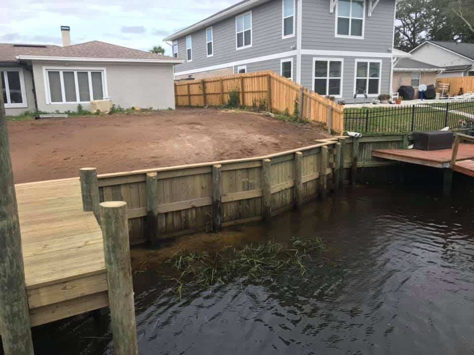 New timber seawall behind two homes with graded dirt yard and adjoining wood dock deck