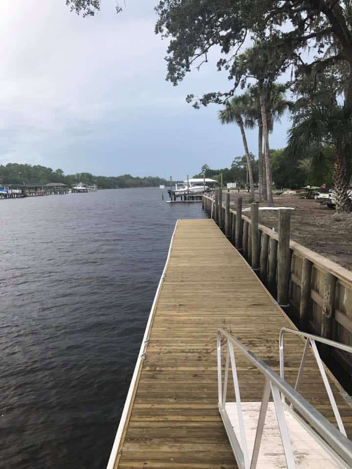 Long wood dock walkway running along a timber seawall and piling row on a wide river