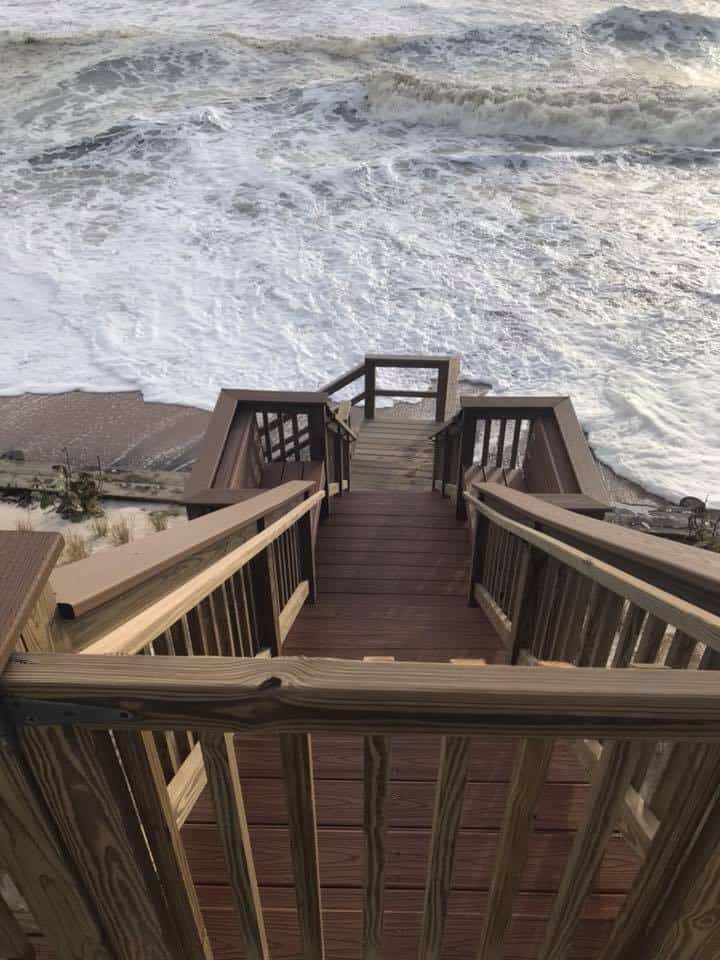 Wooden stairs descending from a deck to a beach with waves breaking close below